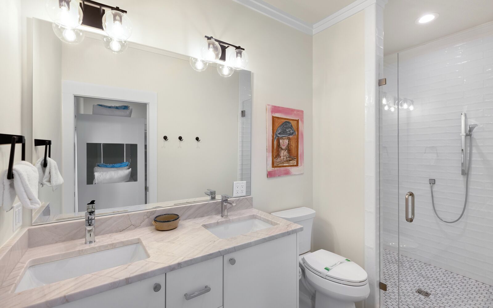 A modern bathroom with a large mirror, two sinks, a toilet, and a shower.