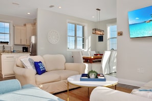 A modern living room with a beige sofa, a coffee table, and a dining area with white chairs.