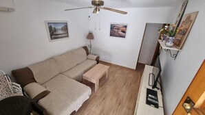 Una habitación con un sofá, una mesita de madera, un ventilador de techo y un escritorio con una computadora.