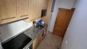 Una cocina compacta con armarios de madera, un microondas integrado y un lavamanos de acero inoxidable.
