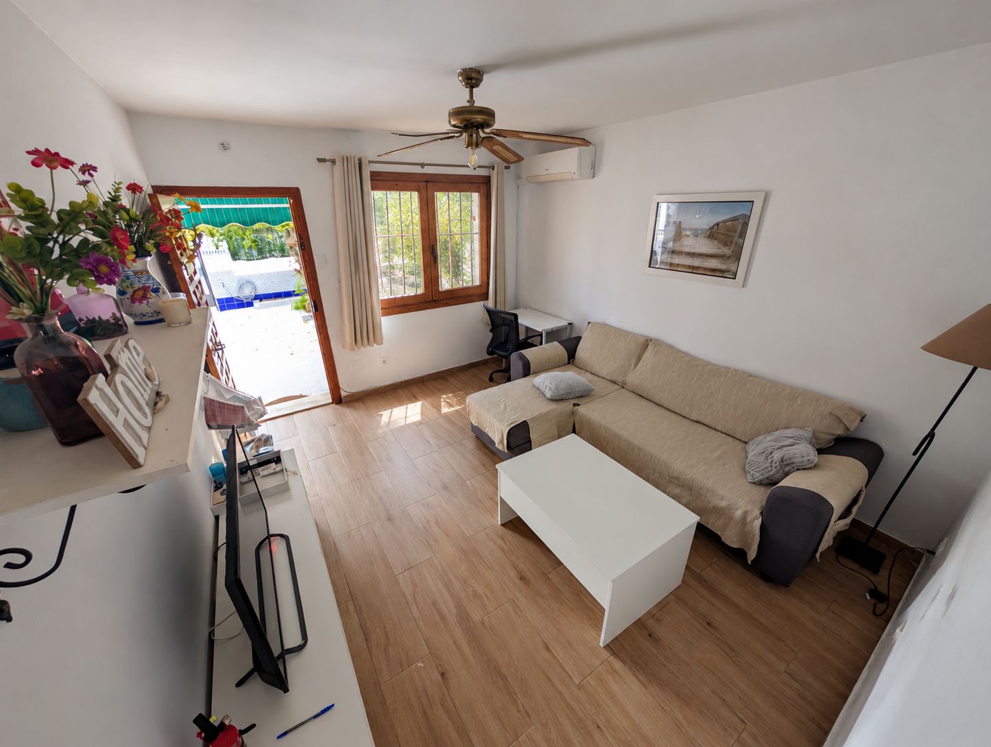A living room with a sofa, a coffee table, a desk, and a ceiling fan.