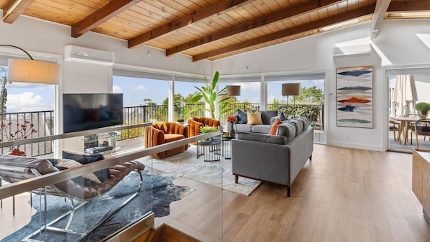 A spacious living area with a wooden ceiling, large windows, a grey sofa, orange armchairs, and a TV. - 180-Degree Ocean Views Deck + Hillside (Half Moon Bay)