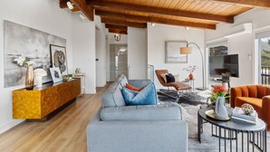 A modern living room with a wooden ceiling, a grey sofa, a coffee table, and a TV. - 180-Degree Ocean Views Deck + Hillside (Half Moon Bay)