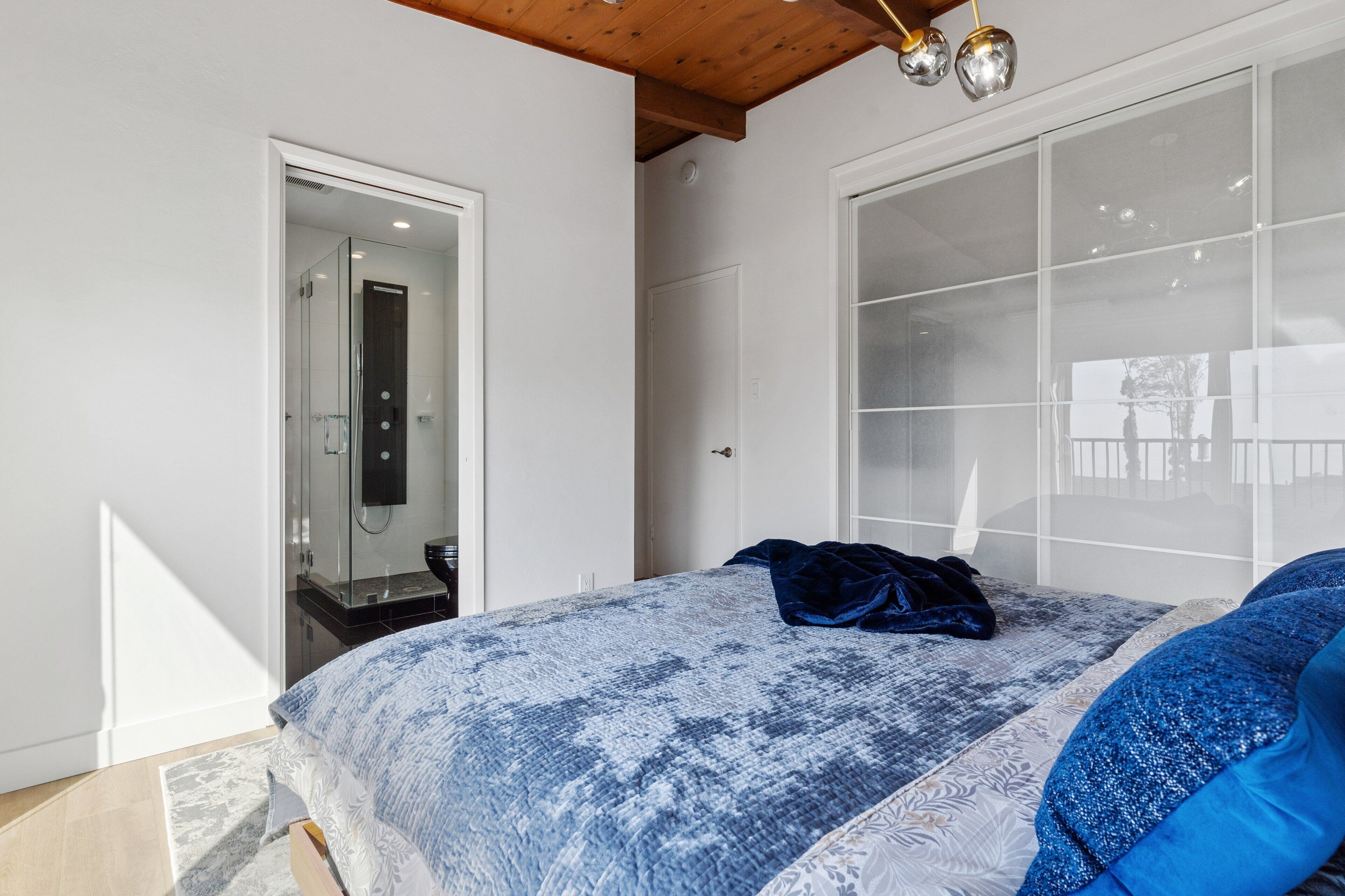 Un dormitorio con una cama grande, un armario y cabina de ducha con mampara de vidrio.