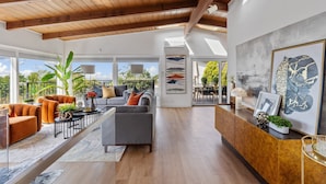 A spacious living area with a wooden ceiling, a grey sofa, orange armchairs, and a dining area with a view. - 180-Degree Ocean Views Deck + Hillside (Half Moon Bay)