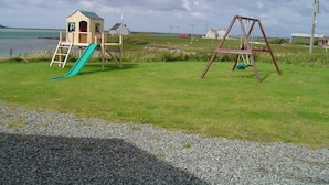 Un terrain de jeux avec un toboggan et des balançoires, situé près d’une étendue d’eau et de maisons.