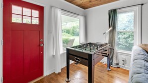 A room with a red door, a foosball table, a white couch, and large windows with curtains. - Relax And Unwind In The Heart Of Fayetteville 2 Bedroom Home (Fayetteville)