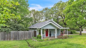 A small house with a red door, a porch, and a fenced yard. - Relax And Unwind In The Heart Of Fayetteville 2 Bedroom Home (Fayetteville)