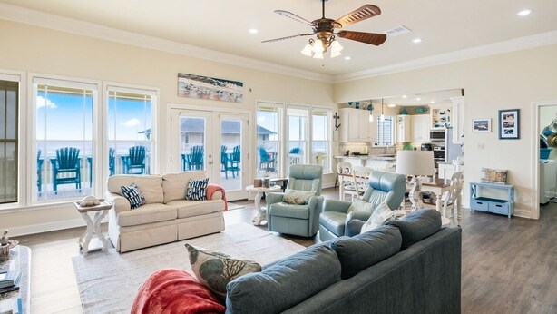 A spacious living room with a large window, a ceiling fan, and a view of outdoor furniture. - Pelican Path 3 Bedroom Home (Port Bolivar)