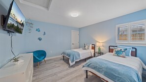 Una camera da letto con due letti, una TV montata a parete, una lampada a soffitto e una finestra con persiane.