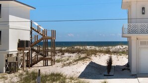A beachfront property with a wooden staircase leading to a balcony, a sandy beach, and a clear view of the ocean. - 🌴☀️Rising Sun | Pet-Friendly Oasis w/ Private Pool + Volleyball Court🏐 (Pensacola Beach)