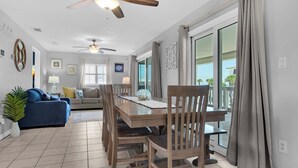 A dining area with a wooden table and chairs, a blue sofa, and a ceiling fan. - 🌴☀️Rising Sun | Pet-Friendly Oasis w/ Private Pool + Volleyball Court🏐 (Pensacola Beach)