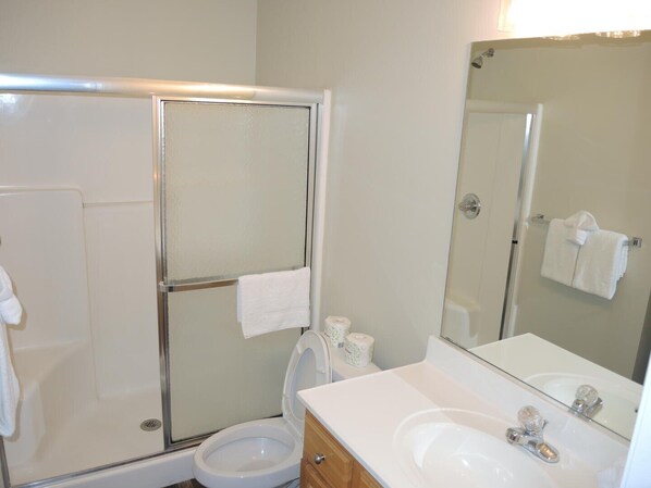 A bathroom with a glass-enclosed shower, a toilet, a sink with a mirror, and a towel rack. - 2703m 1 Bedroom Condo (Calabash)