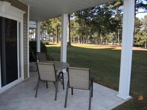 A covered patio with a table and chairs, overlooking a well-maintained lawn and trees. - 2703 2 Bedroom Villa (Calabash)