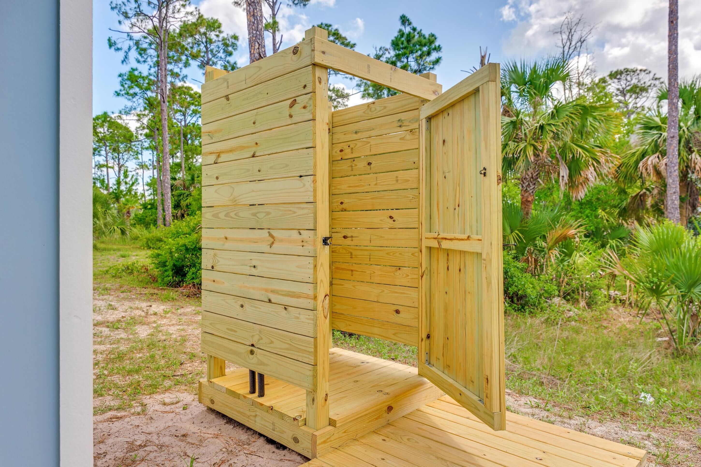 A wooden outdoor shower structure with a door, surrounded by natural vegetation.