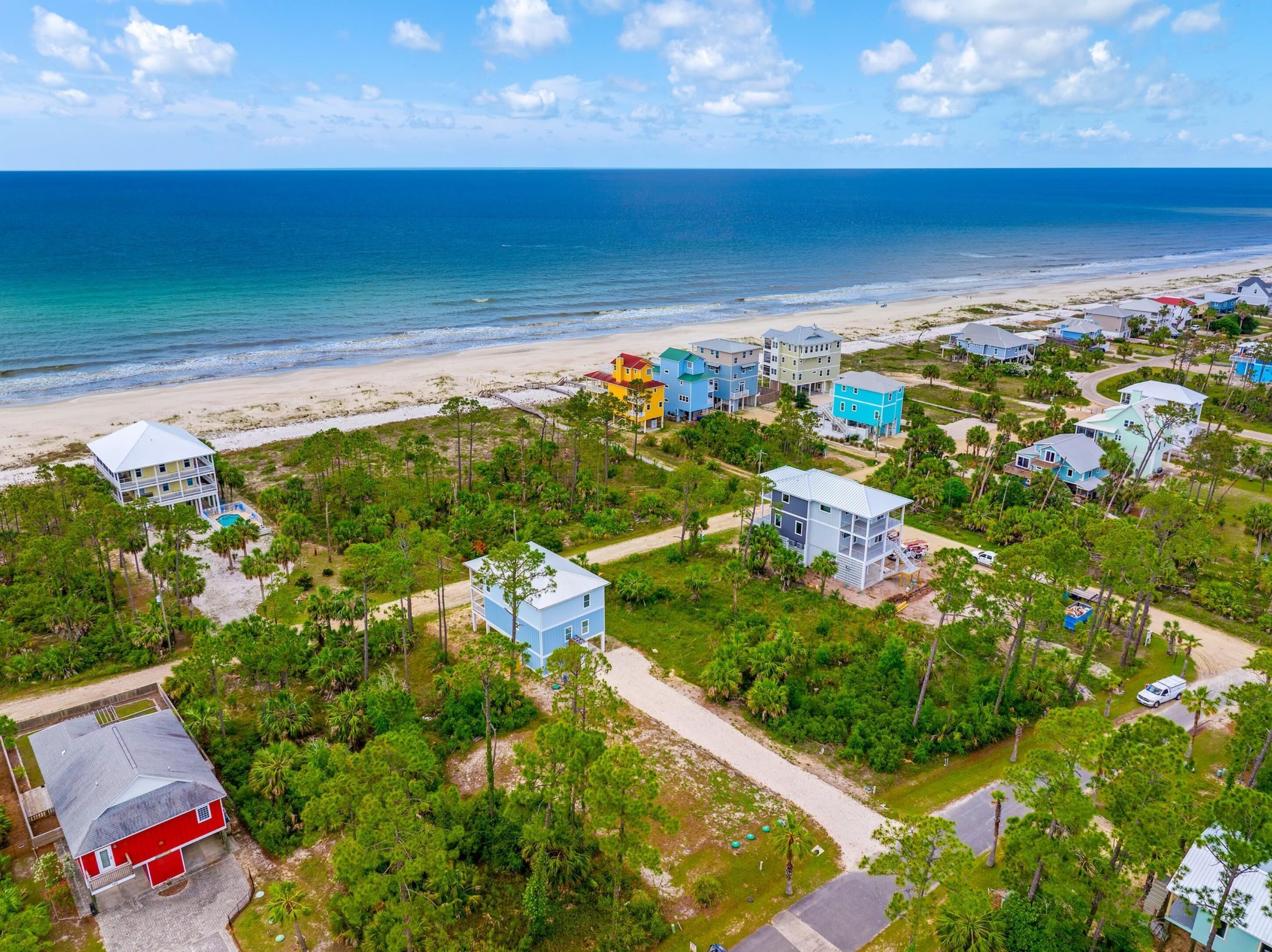 An aerial view of a coastal residential area with houses, a beach, and a clear blue sky.