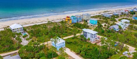 An aerial view of a coastal residential area with houses, a beach, and a clear blue sky.