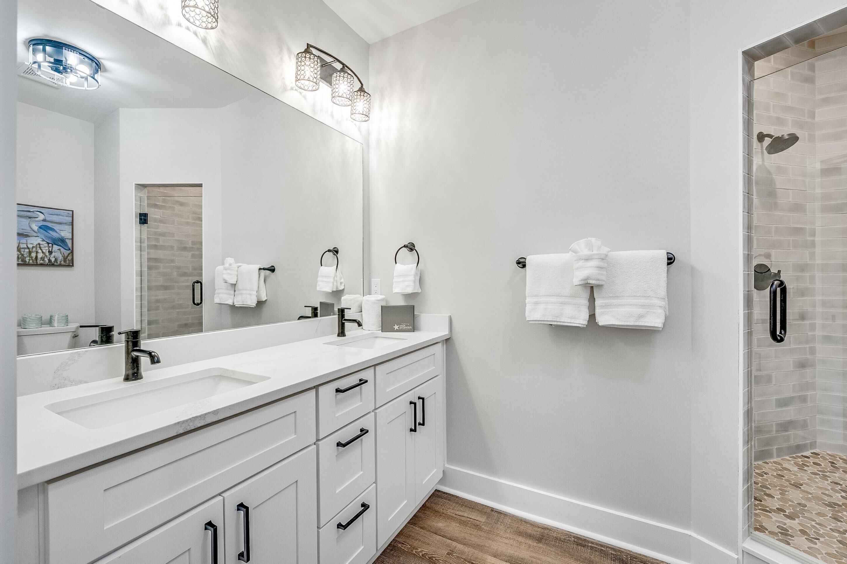 A modern bathroom with a large mirror, two sinks, a shower, and a towel rack.