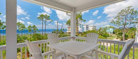 A covered outdoor area with a table and chairs, overlooking a beach and buildings.