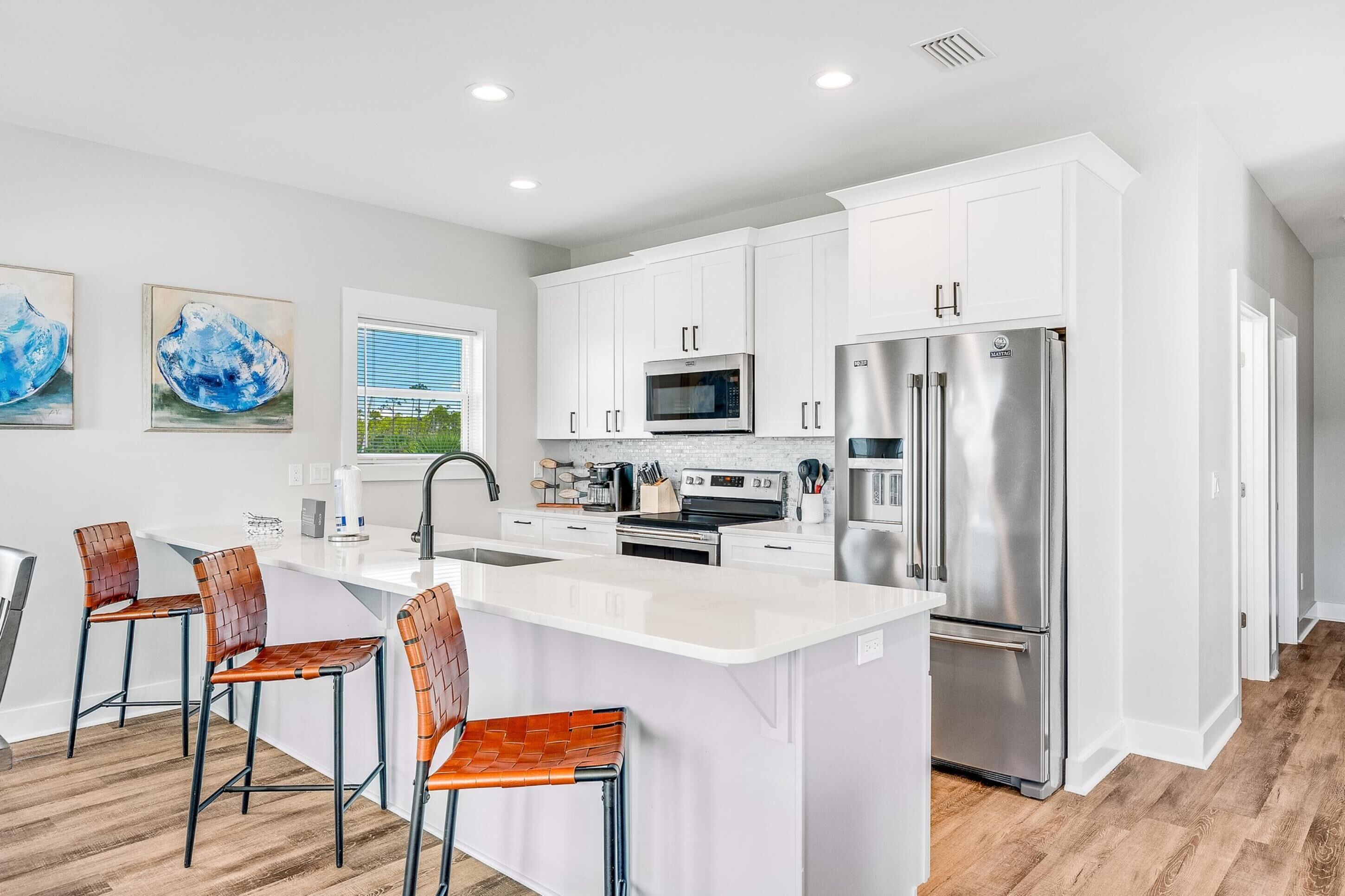 A modern kitchen with white cabinets, stainless steel appliances, and a central island with bar stools.