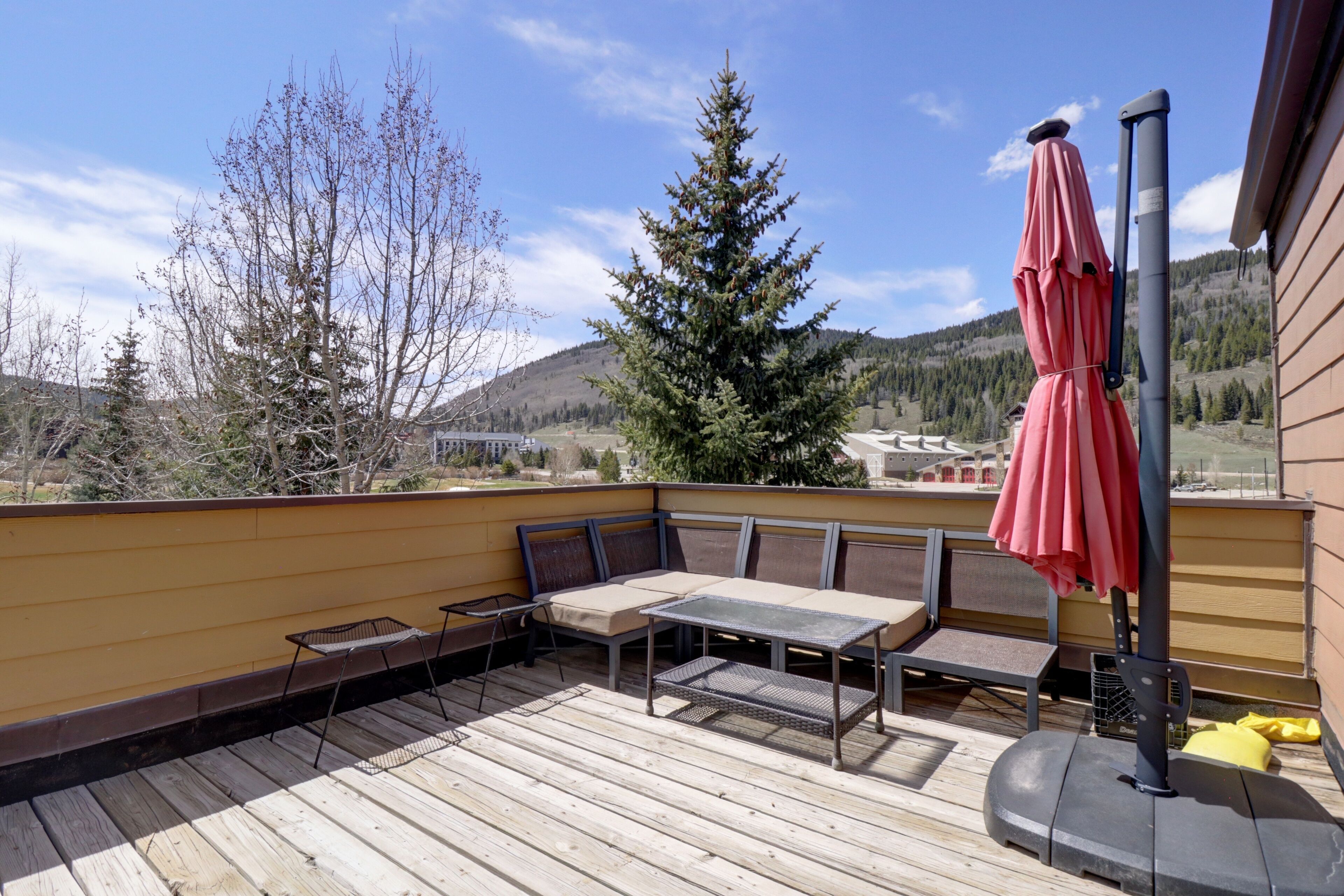 A wooden deck with outdoor furniture, including a sofa and chairs, and a red umbrella.