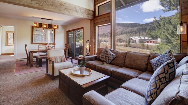 A cozy living room with a large window offering a scenic view, a wooden ceiling, and a dining area with a table and chairs.