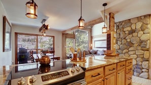 A modern kitchen with a large island, stainless steel appliances, wooden cabinets, and stone wall backsplash.