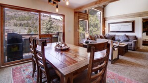 A spacious living area with a wooden dining table, a sofa, and a large window offering a mountain view.