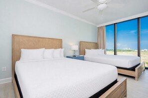 A hotel room with two beds, a ceiling fan, a nightstand with a lamp, and a large window with a view. - Phoenix Gulf Shores Ii 605 4 Bedroom Condo (Gulf Shores)