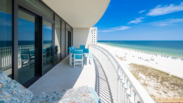 En balkon med udsigt over stranden, en pool og en bygning i baggrunden.
