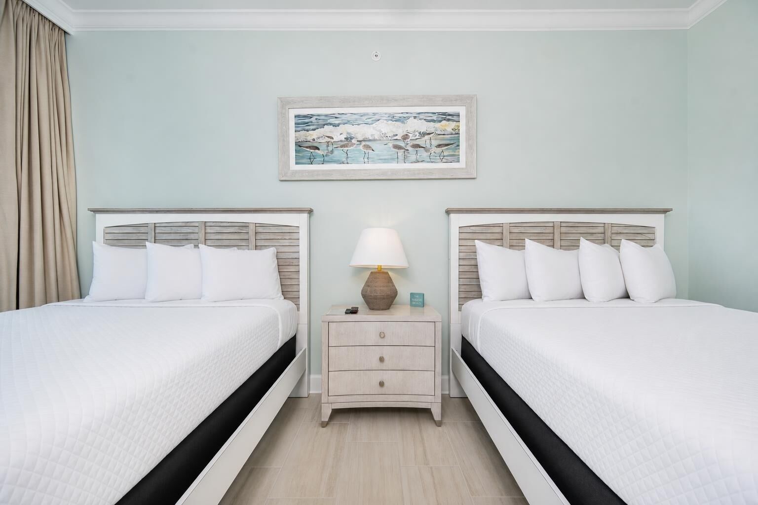 A hotel room with two beds, a nightstand with a lamp, and a painting on the wall.