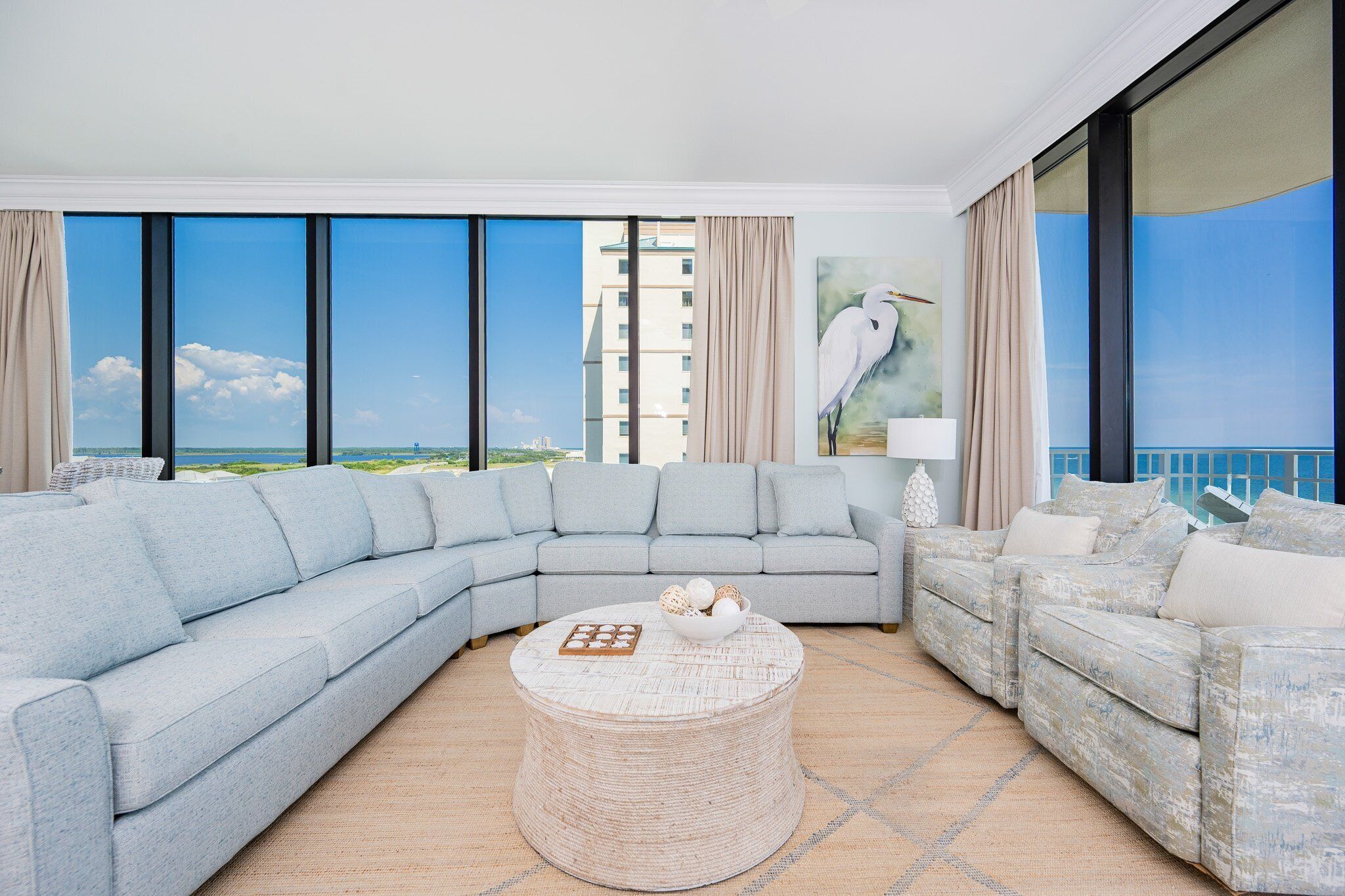 A modern living room with a large L-shaped sectional sofa, a round wicker coffee table, and a painting of a bird on the wall.