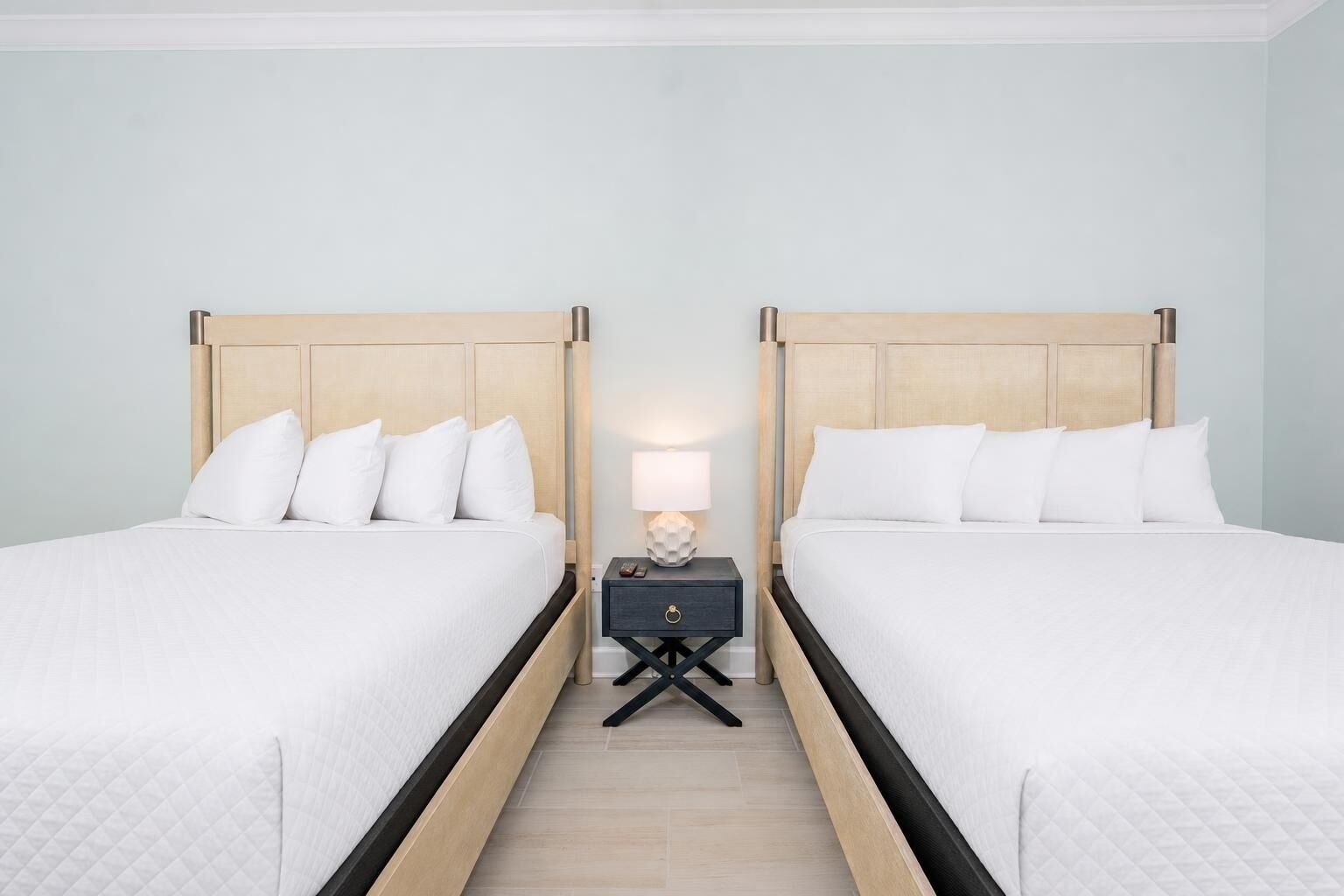 A hotel room with two beds, a nightstand with a lamp, and a wooden floor.