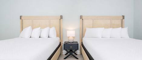 A hotel room with two beds, a nightstand with a lamp, and a wooden floor.