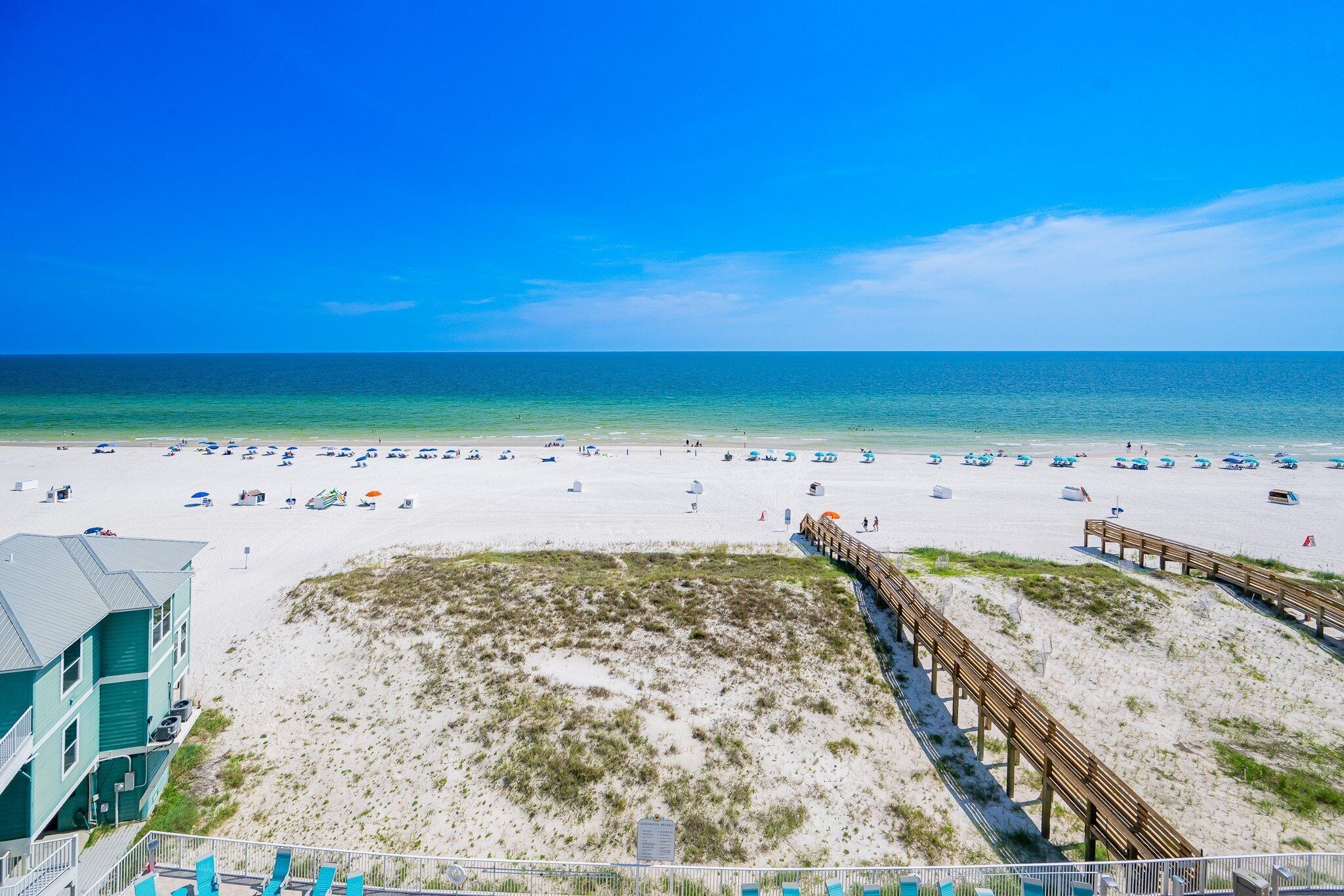 A beach with a wooden boardwalk, beach umbrellas, and a building with a green facade.