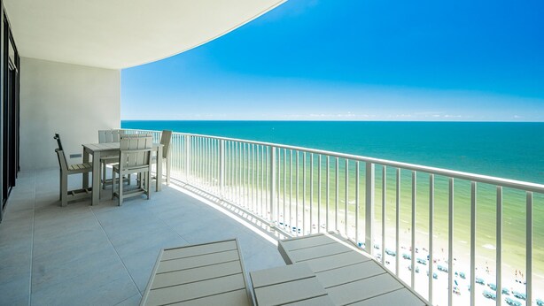 A balcony with a view of the ocean, a table with chairs, and a railing.