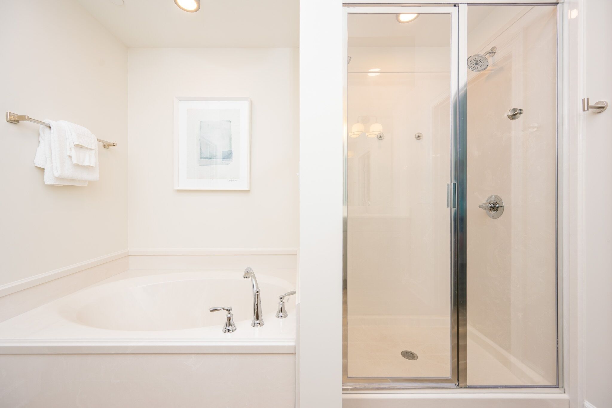 A modern bathroom with a glass-enclosed shower, a standalone bathtub, and a framed picture on the wall.