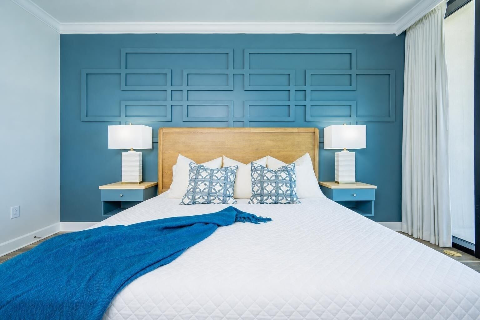 Une chambre d’hôtel avec un grand lit, deux tables de chevet et une tête de lit ornée d’un motif géométrique.