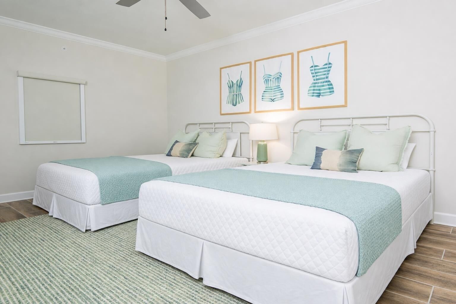 Habitación de hotel con dos camas, ventilador de techo, un cuadro enmarcado en la pared y una alfombra verde.