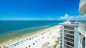 A beach view from a high-rise building with a clear sky, a sandy beach with umbrellas, and the ocean.