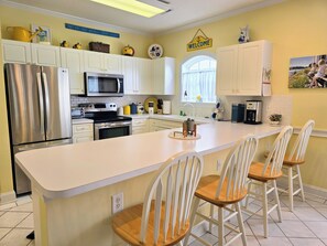 A modern kitchen with white cabinetry, stainless steel appliances, a central island with bar stools, and decorative items on the walls.