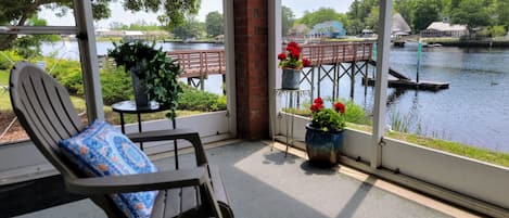 A room with a view of a lake, a chair with a cushion, and potted plants.