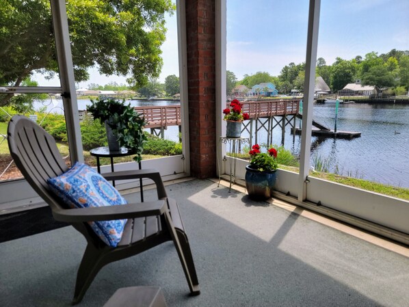 A room with a view of a lake, a chair with a cushion, and potted plants.
