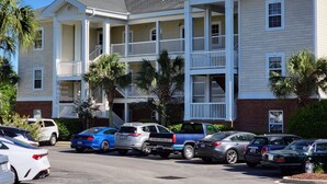 A multi-story building with balconies and a parking lot with various vehicles. - Peaceful 3BR Ground Floor Condo w/ Intracoastal Waterway Views! (Myrtle Beach)