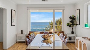 Een eetzaal met een grote tafel, witte muren en uitzicht op zee.