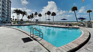 A swimming pool with a curved edge, surrounded by lounge chairs and palm trees, with a building in the background.