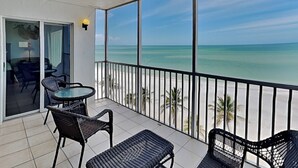 A balcony with a view of the ocean, a table, and two chairs.