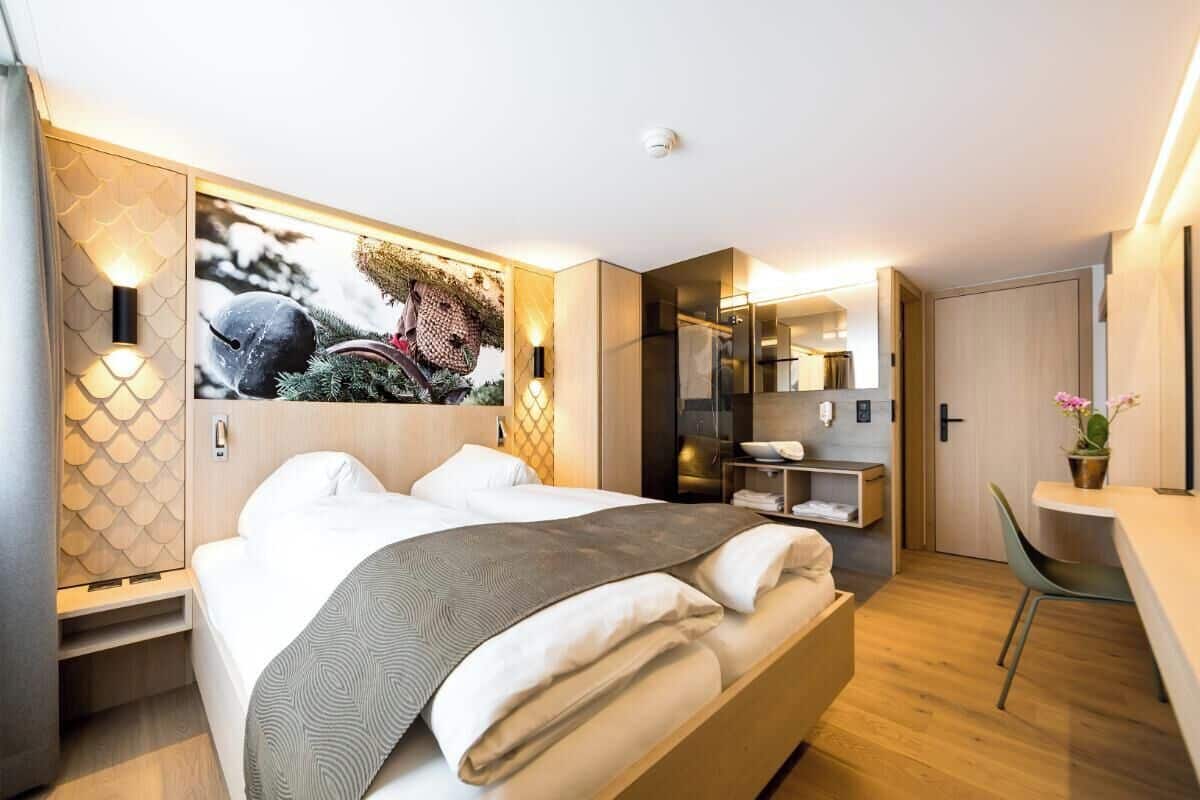 Moderni hotellihuone, jossa on suuri sänky, sisäänrakennettu vaatekaappi, pieni työpöytä ja peili.