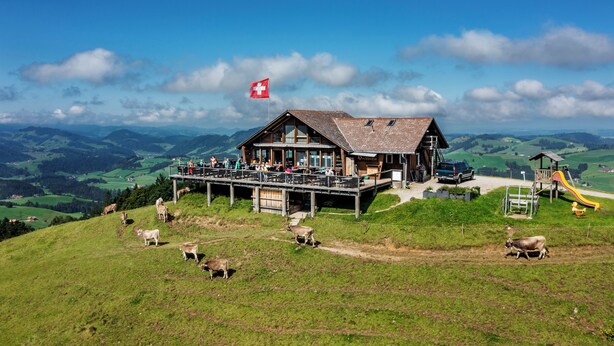 Ein Chalet mit Balkon und Blick über ein Tal, eine Schweizer Flagge und ein Spielplatz.