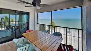 A balcony with a wooden table and chairs, a ceiling fan, and a view of the ocean.